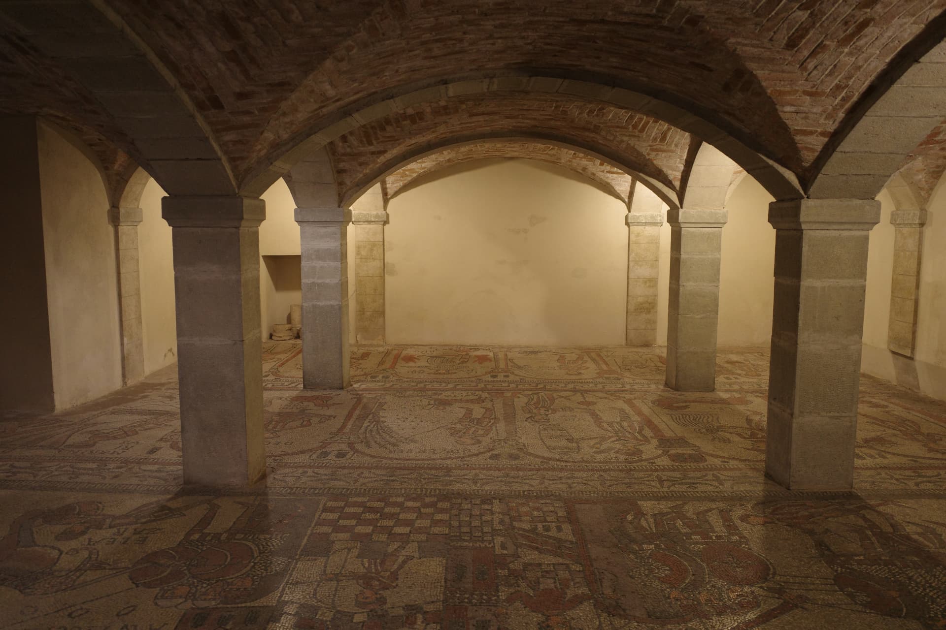 Välvt rum under kyrkan med stenpelare och ett golv av mosaik med figurer och mönster